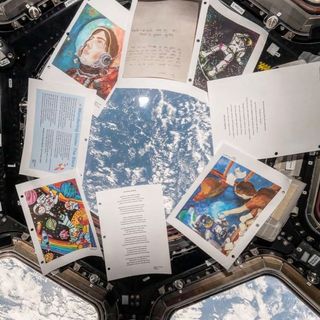 prints of paintings, drawings and poems float against an Earth-facing window aboard a space station