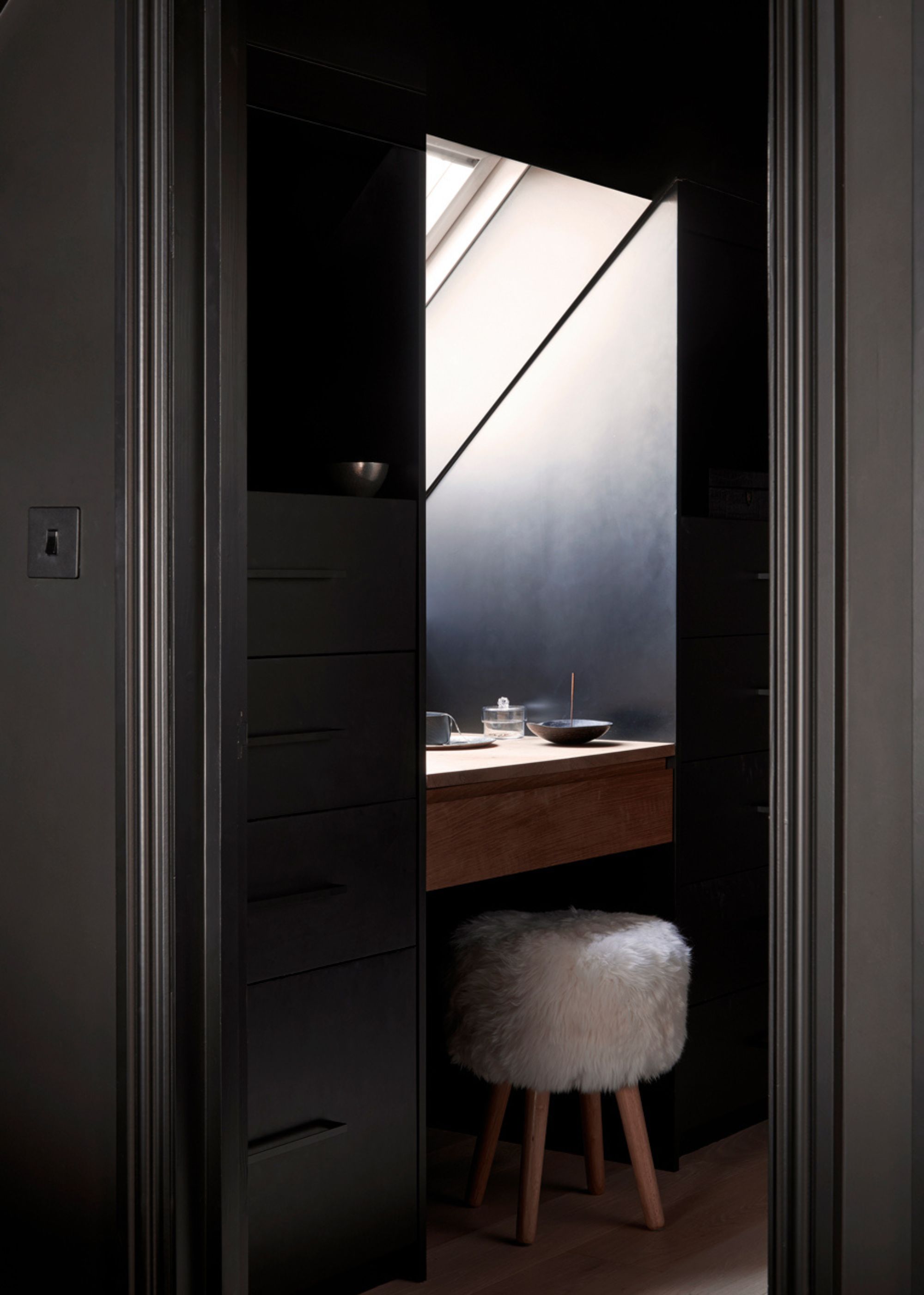 A dark blue vanity with a fuzzy stool, and a skylight
