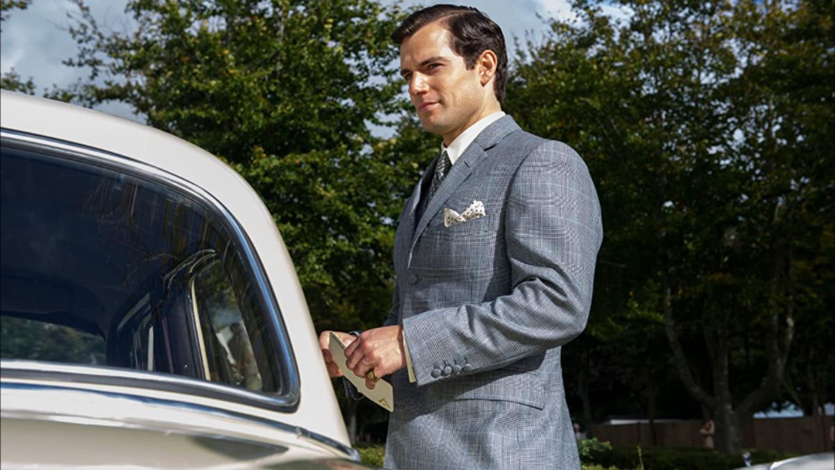 Henry Cavill smiles while standing next to a car in The Man From UNCLE.