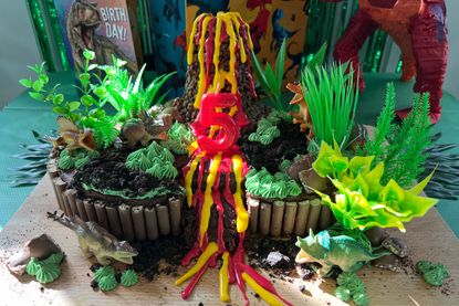 A chocolate cake covered in toy dinosaurs, plastic foliage, cocopops volcano with red and yellow icing