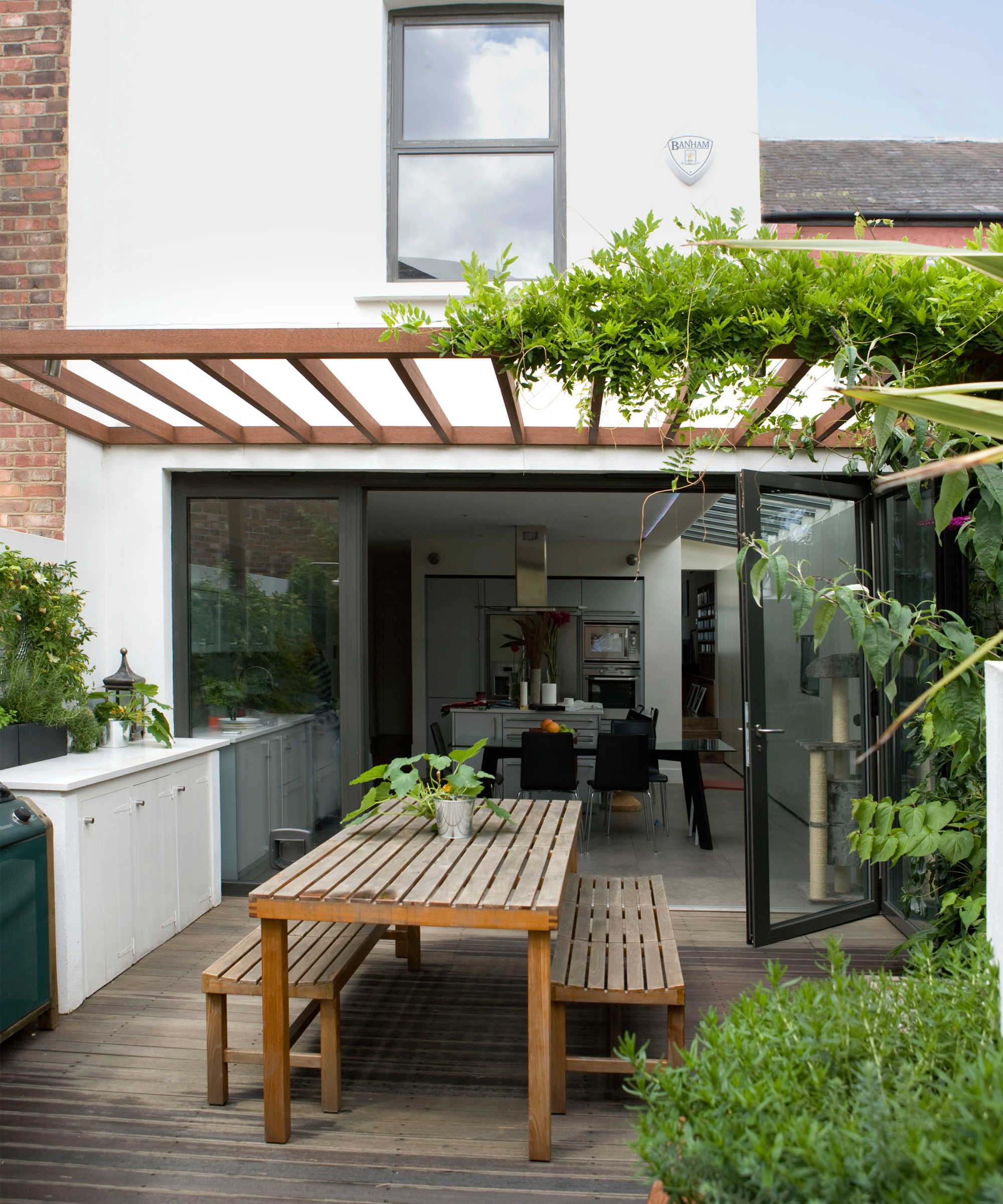 Outdoor dining area in small urban garden with pergola, storage units and bifold doors to the kitchen