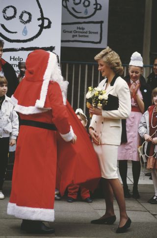 Princess Diana wearing a light pink suit holding flowers and talking to Santa Claus