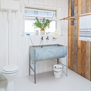 budget bathroom ideas, white bathroom with driftwood wall on right, old fashioned drying hanging rack, vintage galvanised trough style sink, white floor, white painted wall by window