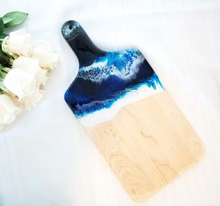 A wood cutting board with blue and white resin that looks like the ocean