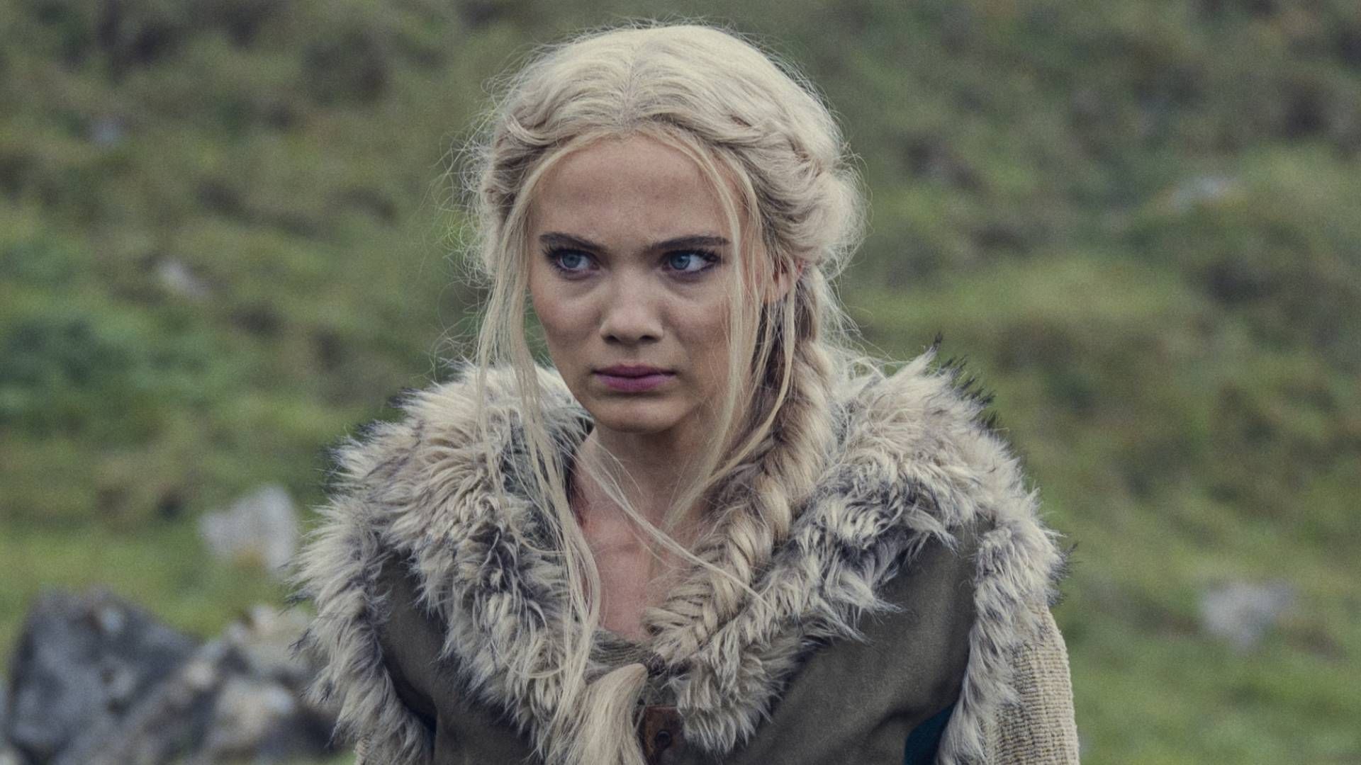 Freya Allan como Ciri em The Witcher, usando um traje com detalhes de pele e cabelos loiros trançados