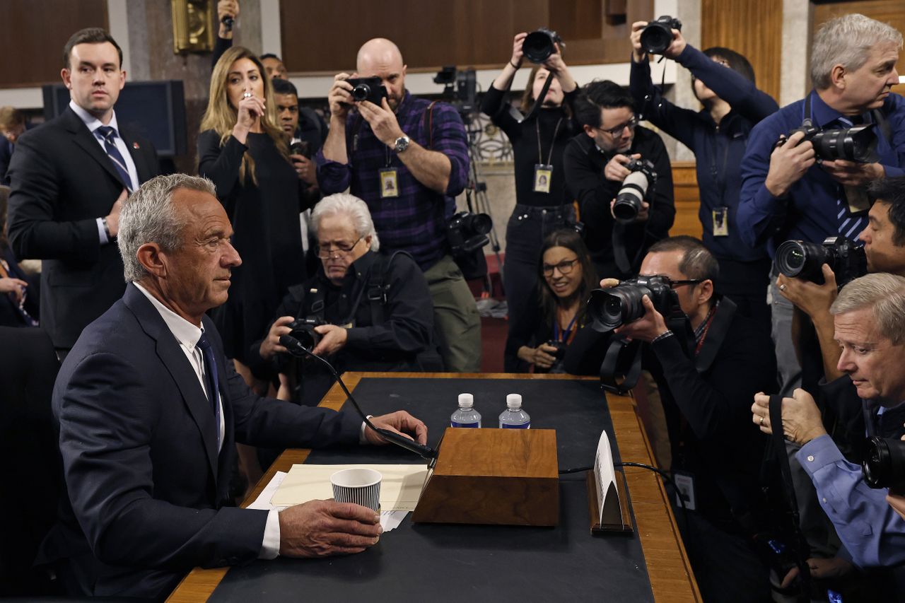 Robert F. Kennedy, Jr. sits at desk for his Senate confirmation hearing, flanked by many reporters.