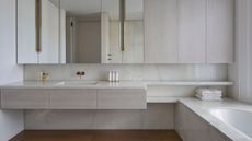 neutral bathroom with floating stone vanity, mirrored cabinets, a built-in bath, and timber flooring