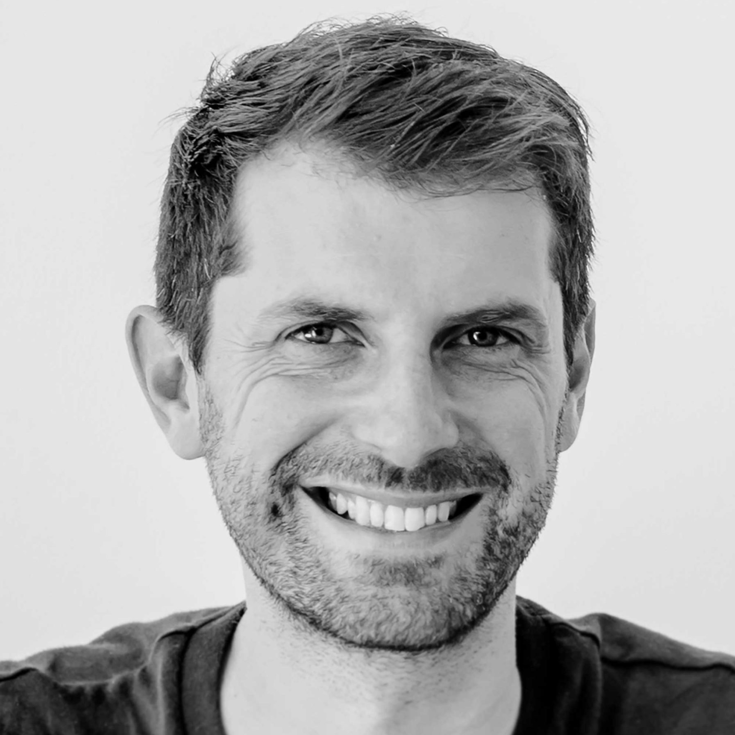 A headshot of a smiling man in black and white