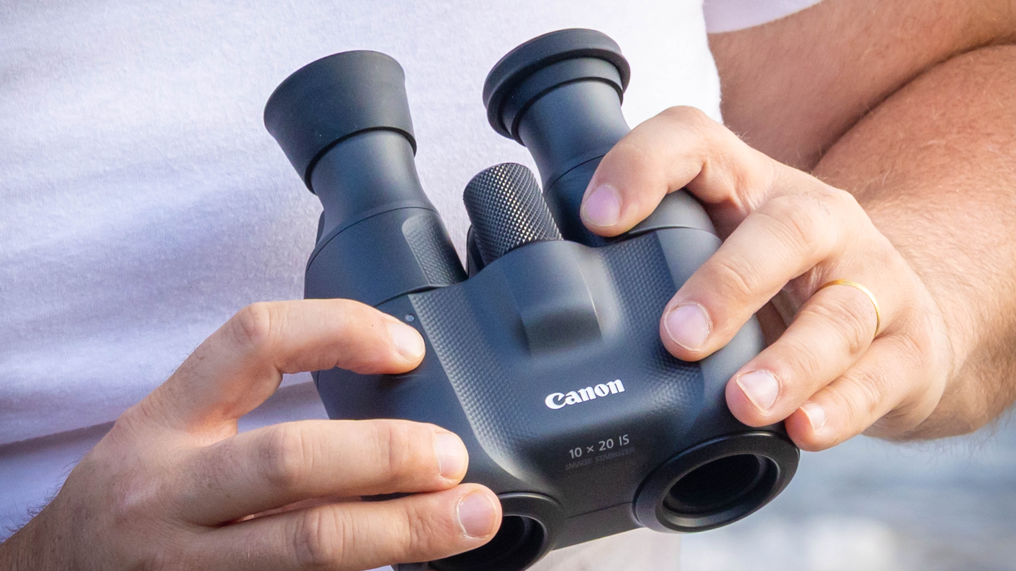 An extreme close-up of the Canon 10x20 IS binoculars being held in someone&#039;s hands.