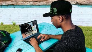 Man in baseball cap using Razer laptop outside