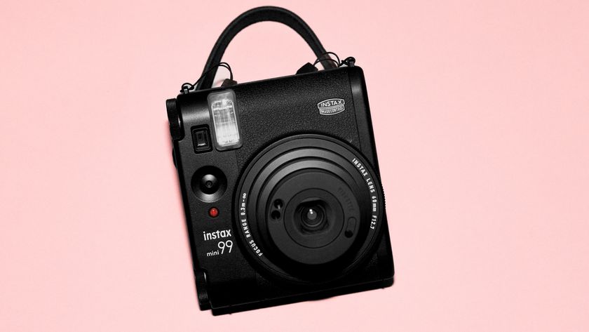 A photograph of the Fujifilm Instax mini 99 in black, set against a pink background.