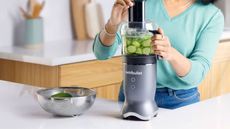 A lady in a mint jumper using the Nutribullet Ultra Plus food processing attachment to slice cucumber