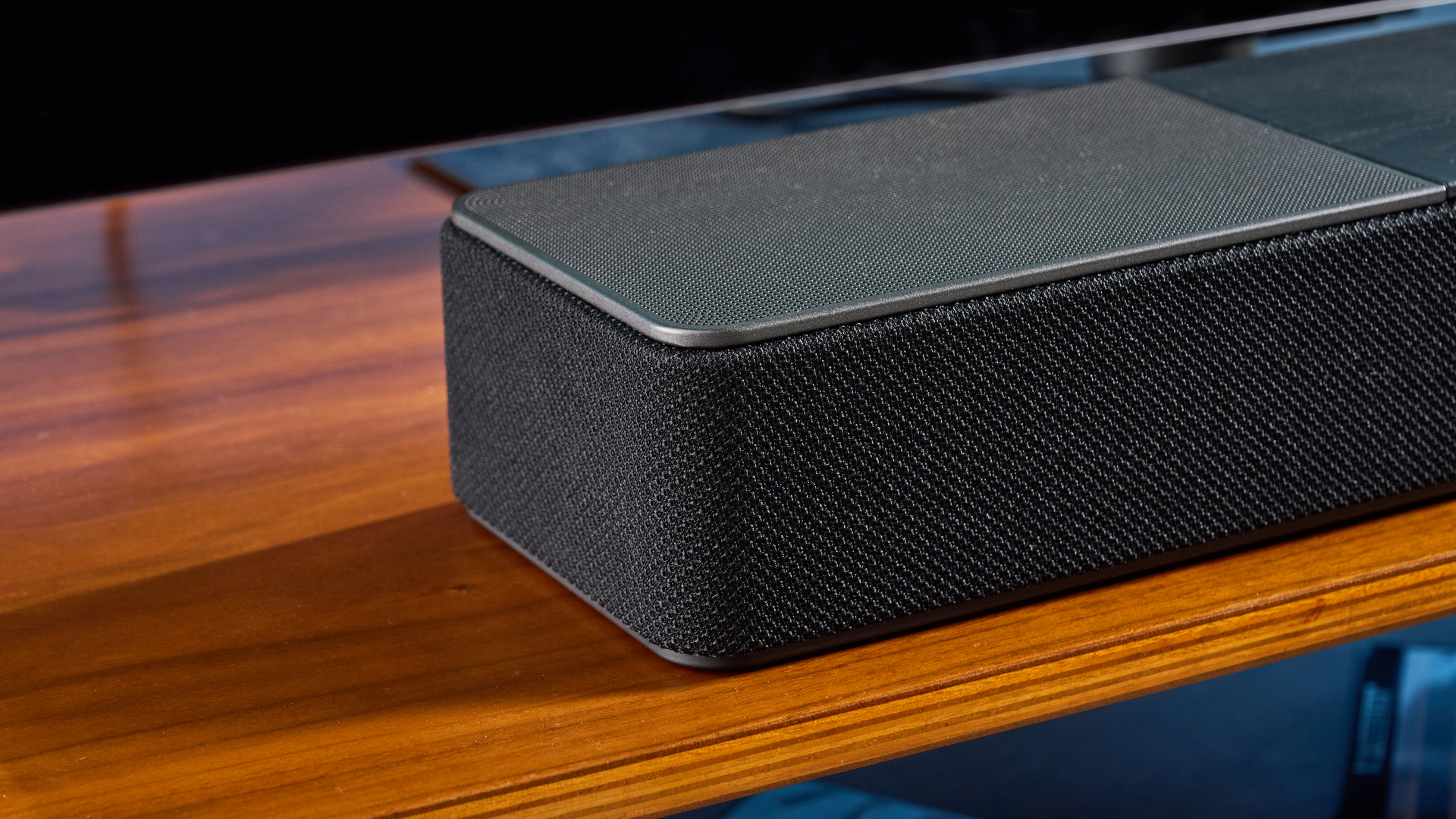 the klipsch flexus core 100 soundbar photographed on a wooden tv stand with a tv behind, showing the remote, buttons, and inputs