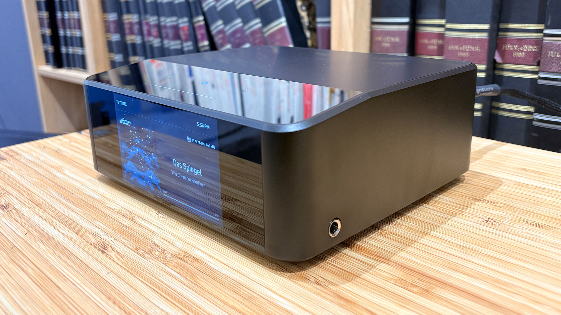 Bluesound Node Icon music streamer on wooden hi-fi rack in front of bookcase