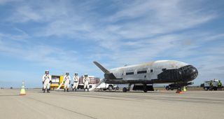 Technicians tend Air Force X-37B space plane after tarmac touchdown.