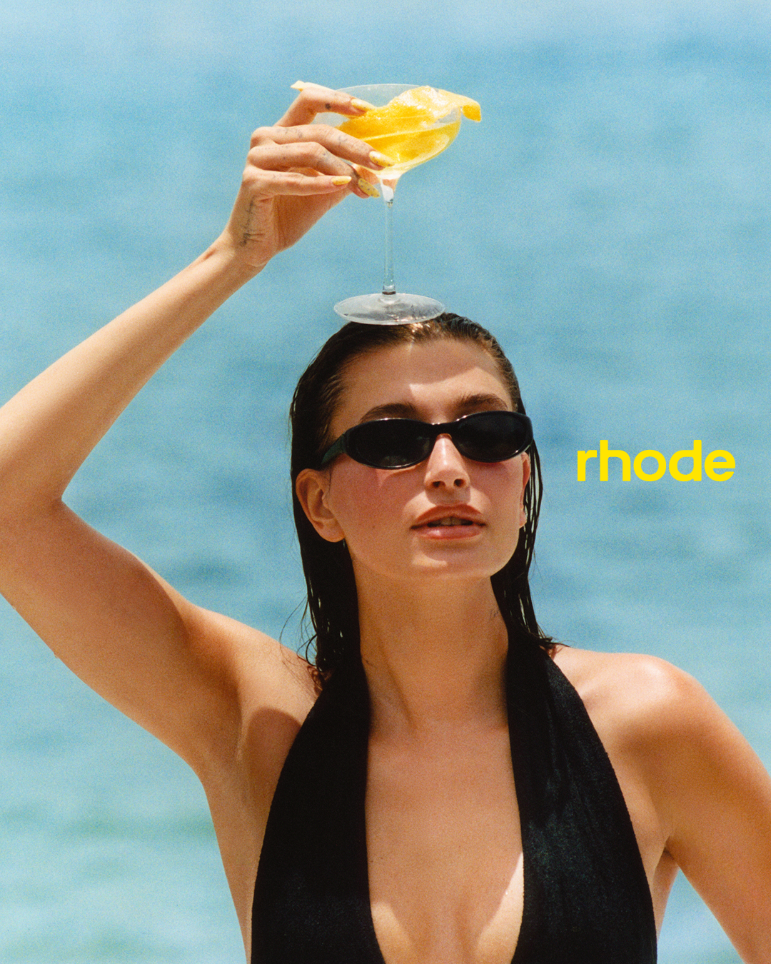 Hailey Bieber poses in the ocean with a lemon drink and Rhode peptide lip treatment