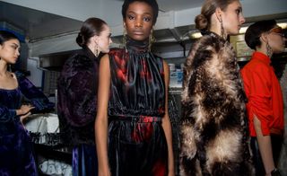 Model is seen wearing a silk, high-neck dress in black and red. Another wears a fur coat in dark and light brown