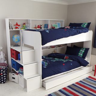 White storage bunk bed with blue bedding and storage space next to multi colored striped carpet
