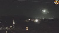 A green fireball is pictured blazing through the night sky above a railway track