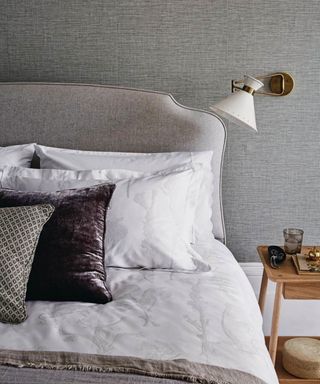 Relaxing and stylish bedroom with grey textured wallpaper, white and brown bedding. A double bed and angled wall light.