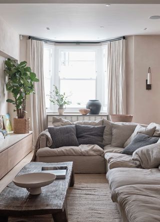 Biege living room with beige curtains, grey cushions and houseplants