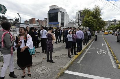People stand in a Quito street following an earthquake.