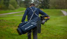 A man walks away from the green with a golf bag on his back