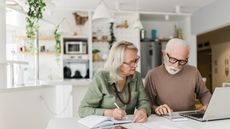 An older couple work together on retirement planning in their kitchen.
