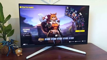 BenQ Mobiuz EX321UX monitor on woodgrain desk with Marvel Rivals character select screen displayed and Squirrel Girl selected.