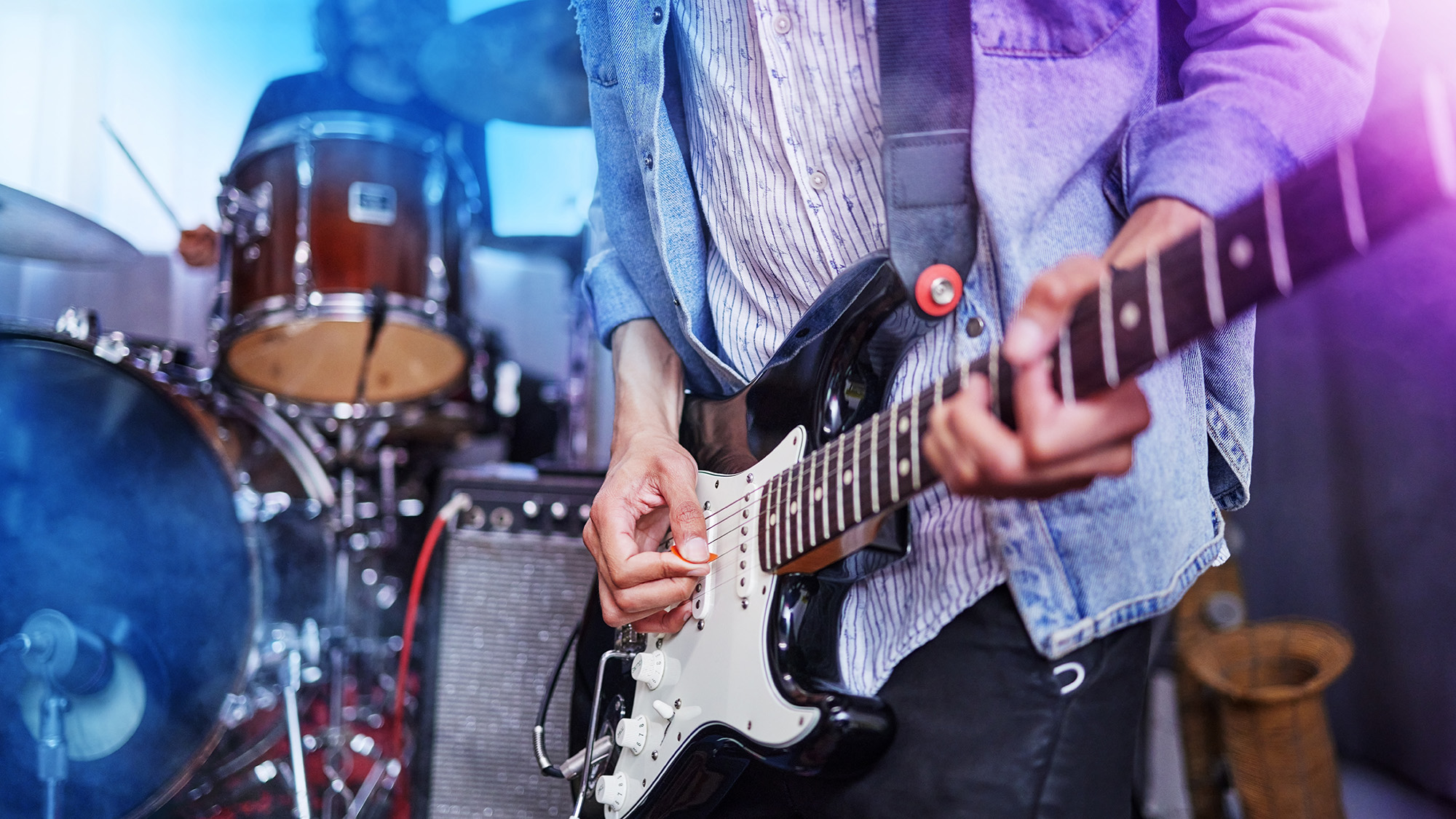 Male guitarist performing on stage with his bandmates in the background