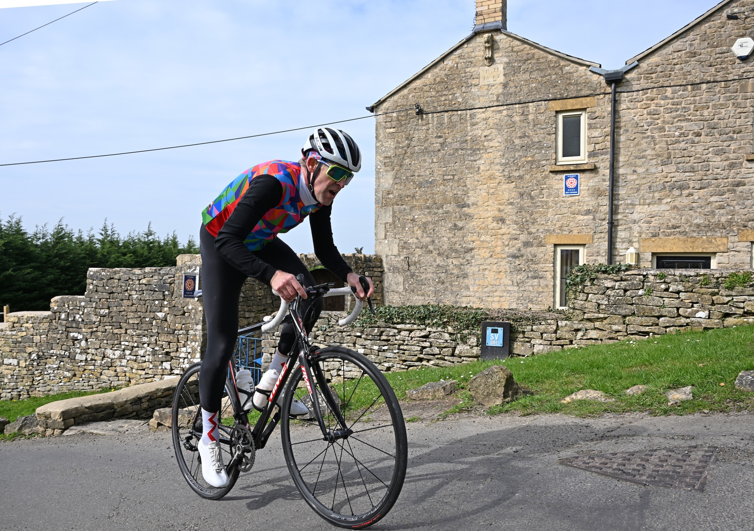Simon Warren climbing out of the saddle, with stone houses in the background