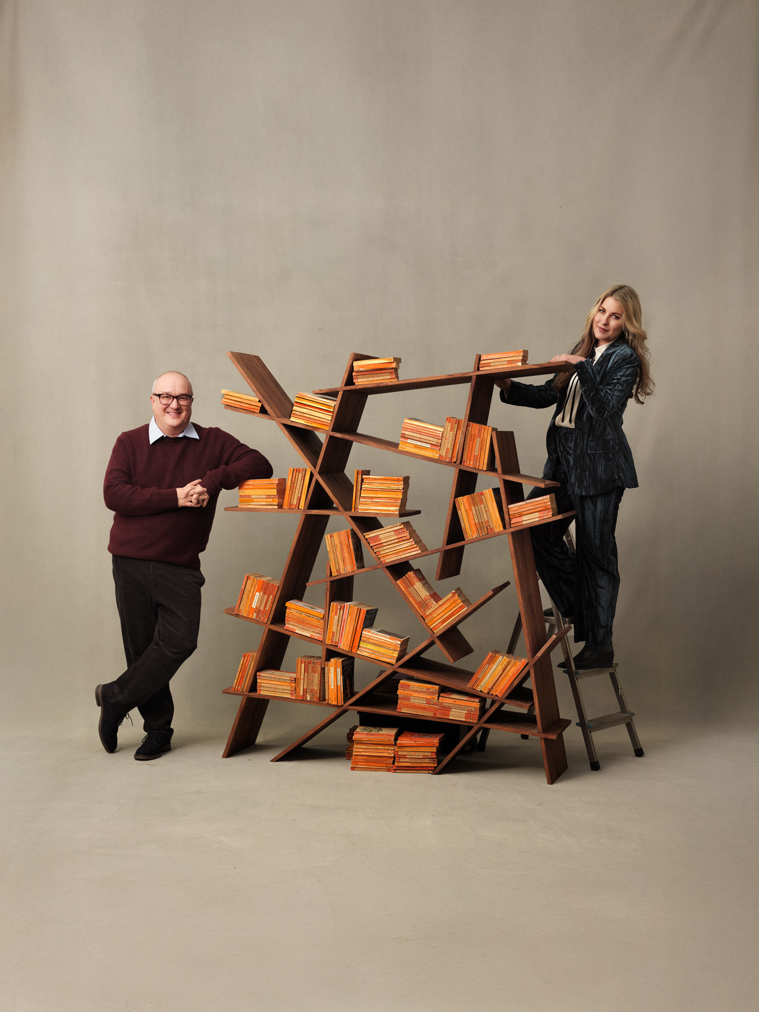 Dominic Sandbrook and Tabitha Syrett leaning against a bookshelf in a studio with orange (penguin classics) book bindings