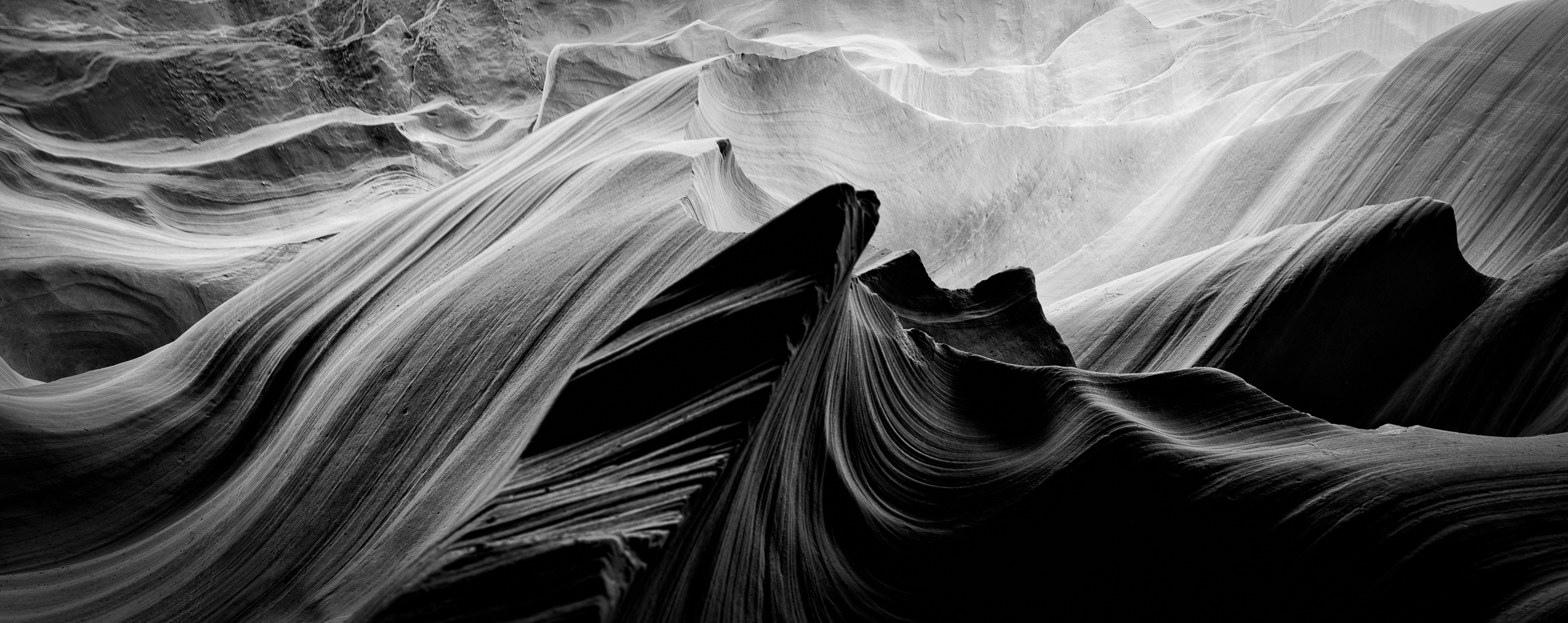 A close-up view of textured, wavy sandstone formations in black and white, highlighting the play of light and shadow in a narrow canyon
