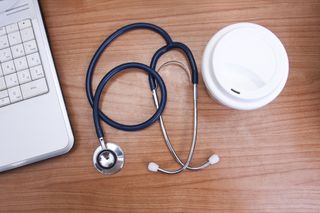 Stethoscope next to keyboard and coffee cup