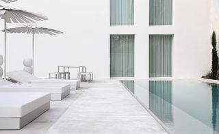 An all-white concrete pool sits within a classically-landscaped outdoor area