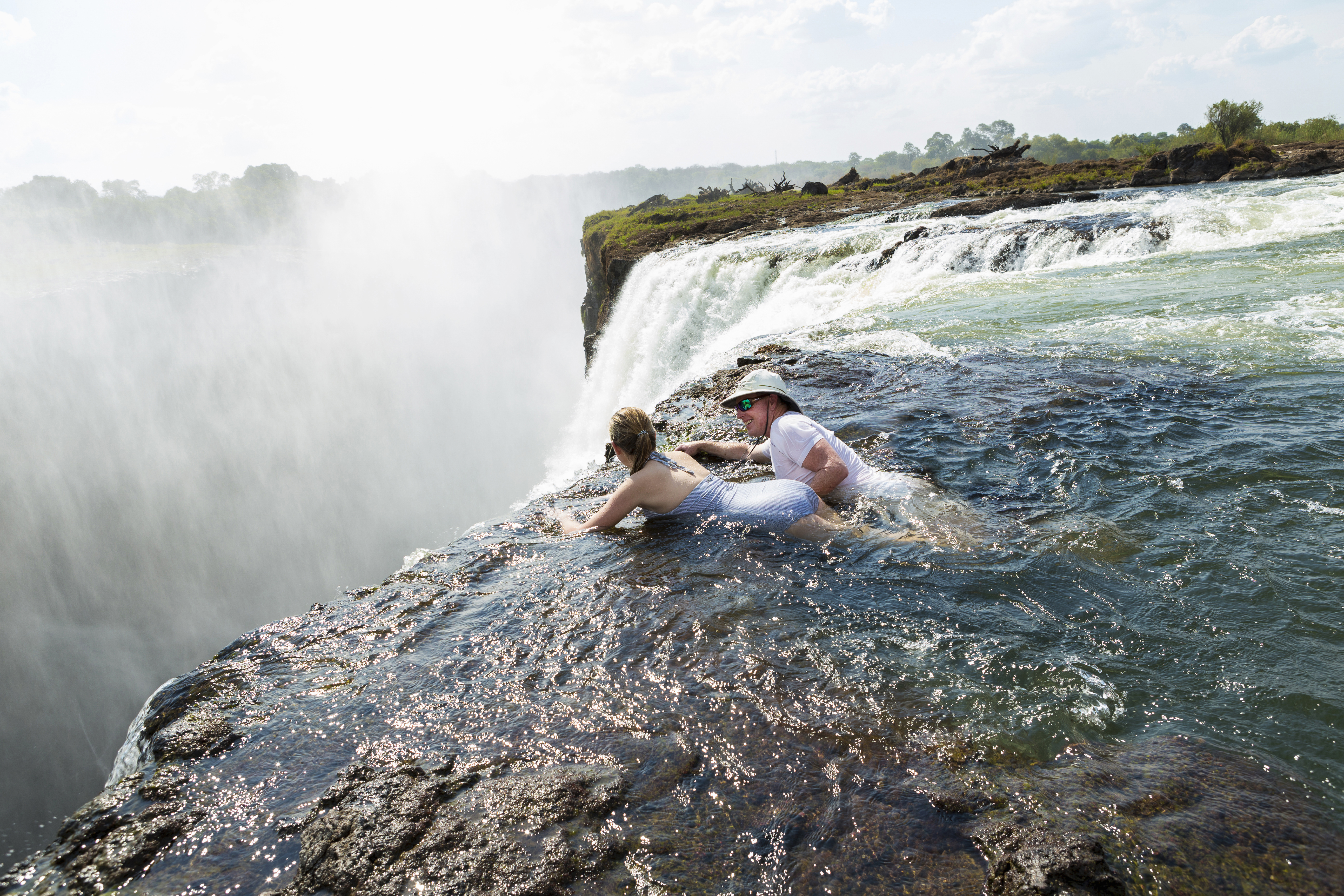 A father and daughter swim in the Devil's Pool at Victoria Falls