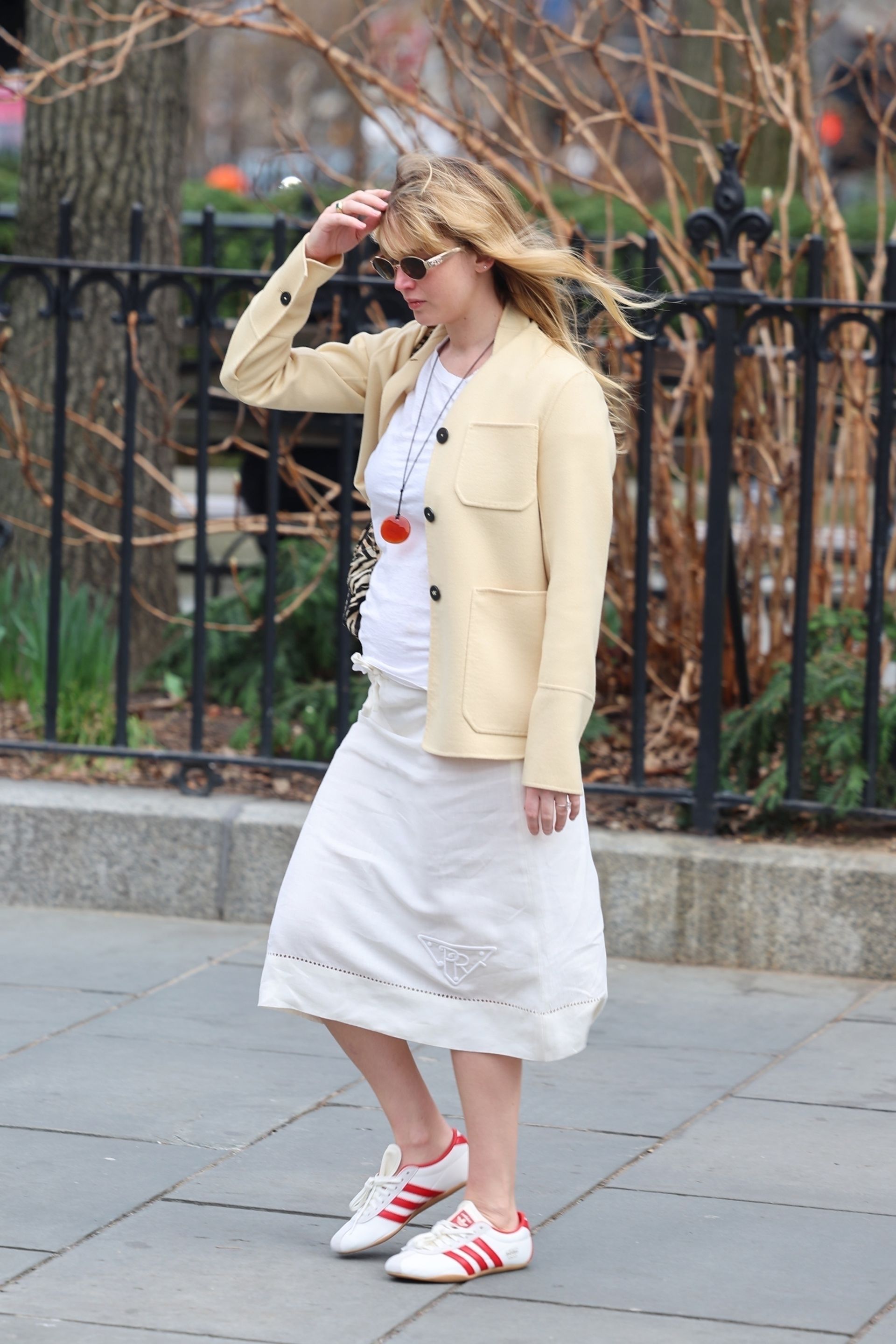 Jennifer Lawrence pictured in a pair of Adidas Tokyo trainers, a cream Prada midi skirt, a white top and a cashmere butter yellow jacket. She accessorises the look with a red rope necklace and Celine Triomphe sunglasses in a recent image taken of her.