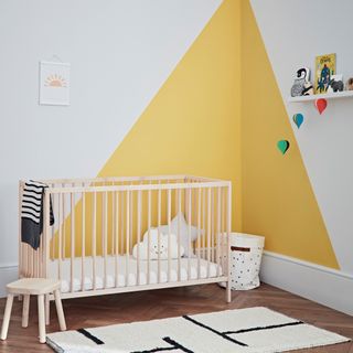 Yellow triangle and grey wall, wooden crib with cloud pillow on wooden floor with white rug