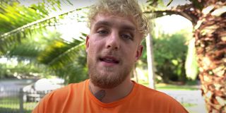 Jake Paul with an orange shirt on standing in his front yard and talking directly to a camera very close to his face.