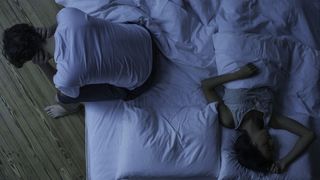 man awake in bed while his partner sleeps