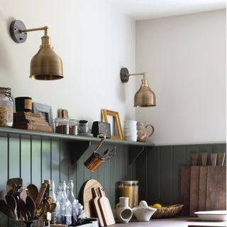 bronze wall lights over green panelled kitchen wall and shelf with wooden worktop