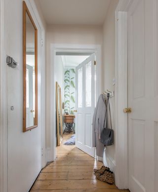 White hallway with wooden framed square mirror and clothing hooks with jacket and grey handbag hanging on it