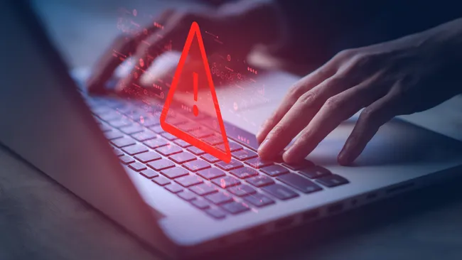 Hands on a laptop with a warning exclamation point