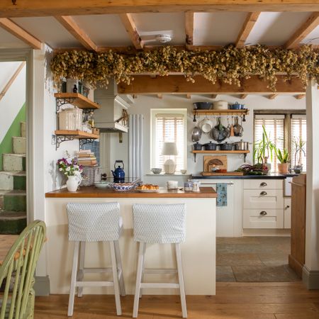 Cottage open plan kitchen diner with cream kitchen units, breakfast bar and hops hanging from ceiling