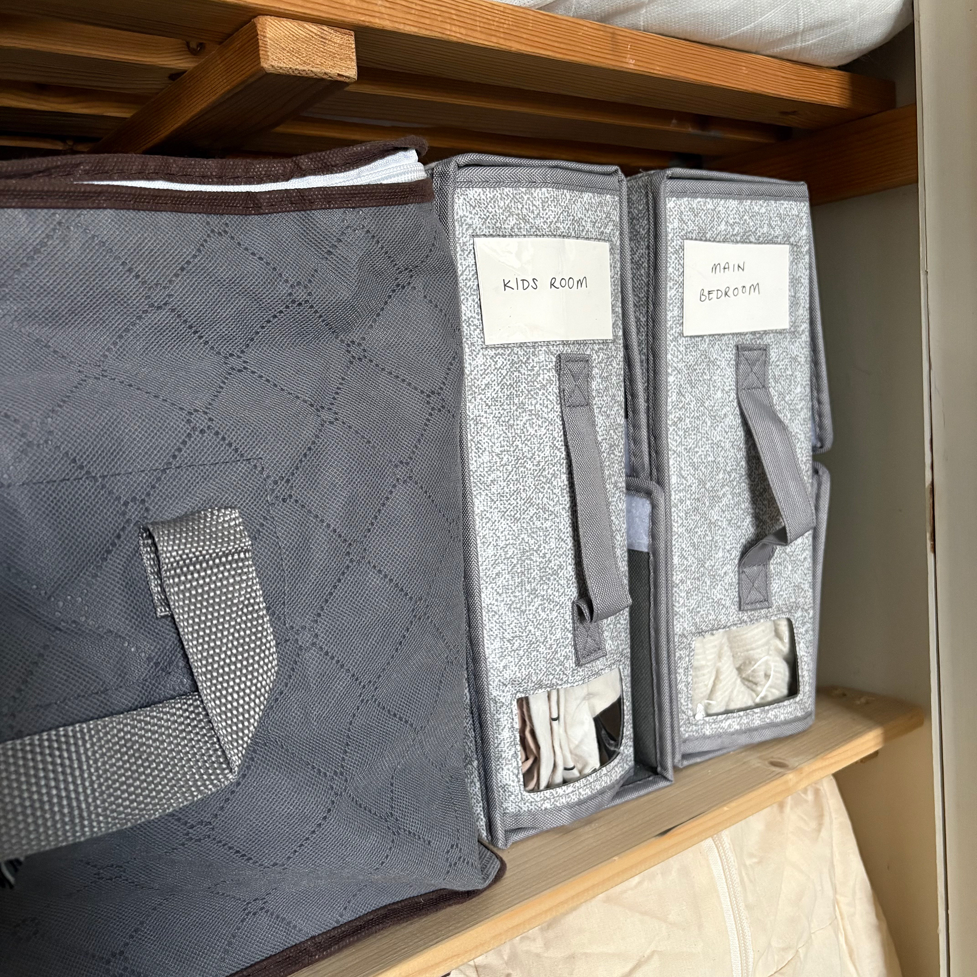 Two grey bedding organising boxes stacked vertically with window showing bedding inside and labels at the top