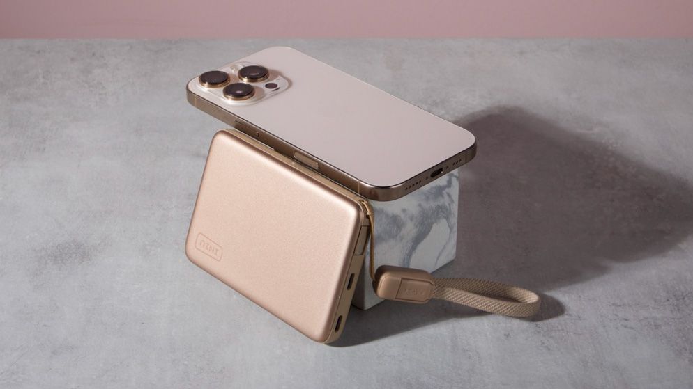 An Iniu SnapGo Air 10000mAh Power Bank leant against a marble block with an iPhone 16 Pro resting on top of it.
