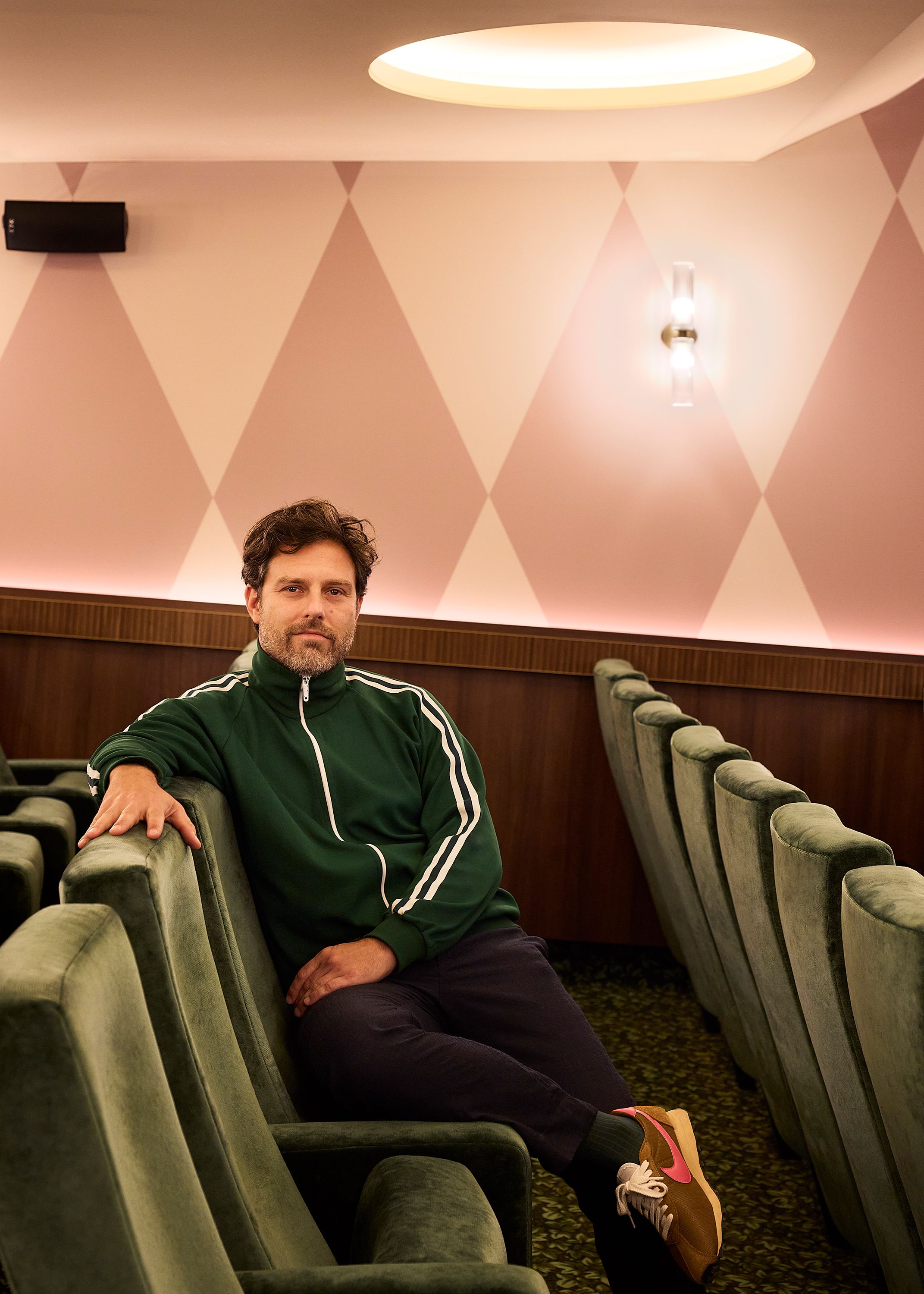 A series of interior shots depicting the retro-futuristic decor of a cinema captures velvet-clad rooms with a palette of reds, pinks, and pale dark greens, theatrical doorways, either arched or draped in curtains, ceiling porthole windows, and a vintage, golden entrance with red neon lights.