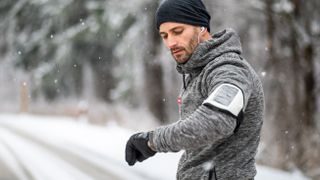 Man checking sports watch while running on a snowy winter day
