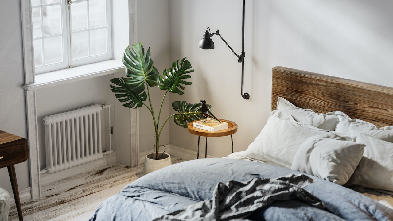 small bedroom with a blue comforter and a wooden headboard next to a window with a bedside lamp on