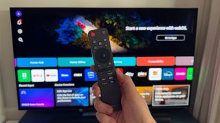 LG's new Magic Remote held in a hand in front the LG G5 OLED TV.